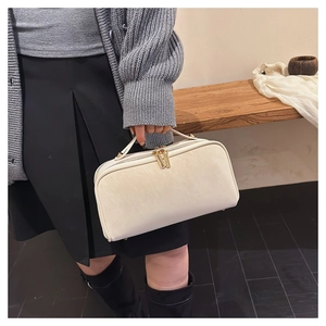 Détail de la trousse de toilette crème avec zips dorés et poignée en cuir souple