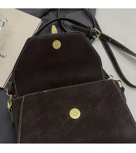 Detail of dark brown crossbody bag featuring white contrast stitching and magnetic buckle