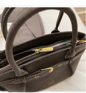 Detail of premium textured dark brown leather bag with smooth golden zipper and brand logo