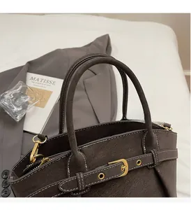 Detail of dark brown dumpling bag with white contrast stitching and gold buckle accents