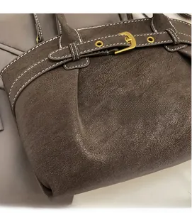 Close-up of dark brown suede bag with white stitching and gold metal buckle detail