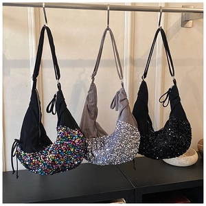 Three sequined crescent bags in iridescent, silver, and black hanging on display