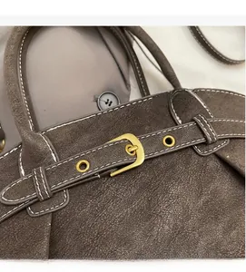 Detail of dark brown suede handbag with white stitching and gold buckle accents