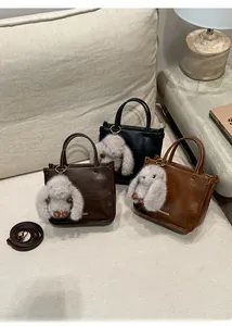 Three vintage square handbags in various colors with plush rabbit charms on a sofa