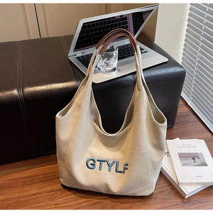 Detail of beige canvas tote with blue 3D GTYLF embroidery and brown leather handles