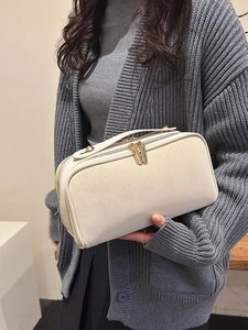 Grande trousse de toilette en cuir crème avec zips dorés tenue par un mannequin