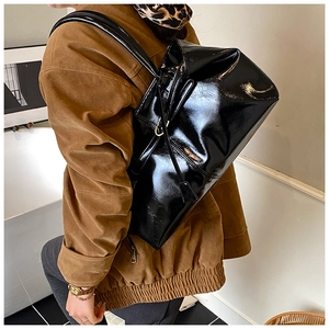 Close-up of a large black glossy patent leather tote bag styled on a model's shoulder