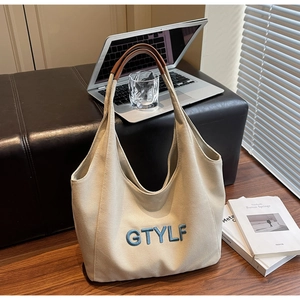 Close-up of cream canvas tote bag with blue GTYLF embroidery and brown leather handles