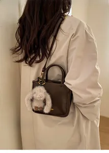 Deep brown square crossbody bag with cute plush rabbit charm on model's shoulder