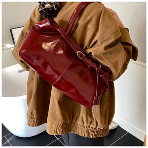 Detail of a burgundy glossy patent leather shoulder bag with gold metal buckle