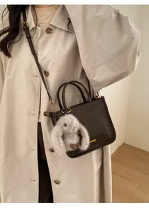 Detail of dark brown leather bucket bag with cute plush bunny charm and golden hardware
