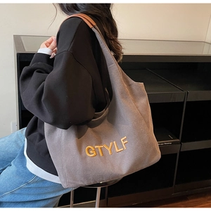 Detail of GTYLF canvas tote bag with yellow embroidery and leather shoulder straps