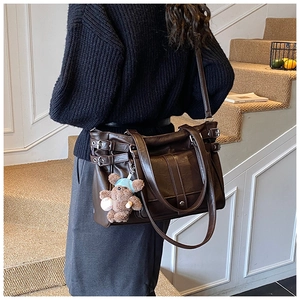 Detail of dark brown leather tote bag with side buckles and cute bear charm pendant