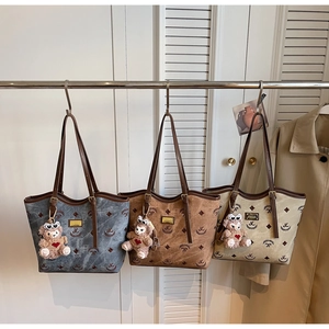 Detailed view of embroidered tote bags in blue, brown and beige with plush bear charms
