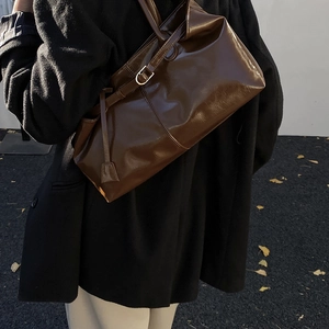 Close-up of deep brown glossy leather handbag with long shoulder strap in outdoor setting