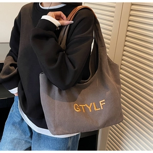 Detail of dark grey canvas tote bag with brown leather straps worn by a model