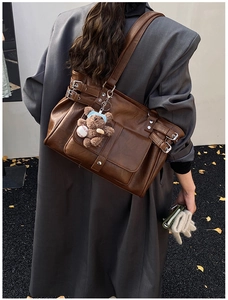 Close-up of brown vintage leather tote bag with metallic buckles and cute bear charm