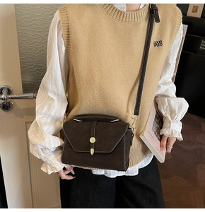 Detailed view of dark brown suede crossbody bag with gold buckle and stitching