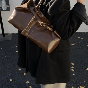 Detail of dark brown glossy patent leather tote bag with elegant gold metal buckle hardware