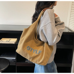 Detail of yellow canvas tote bag featuring embroidered letters and leather strap