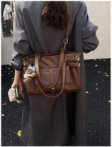Detail of dark brown vintage tote bag with side buckles and teddy bear charm on model