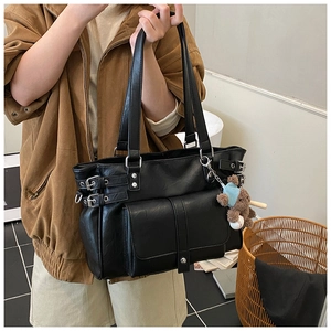 Detail of black leather tote bag with utility pockets and a cute bear keychain accessory