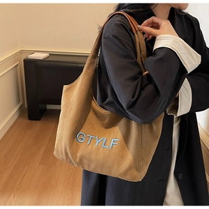Detail of a large brown suede tote bag featuring blue GTYLF embroidery on the front
