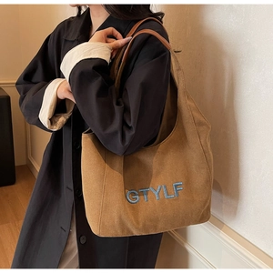 Caramel brown canvas tote bag with blue embroidered letters worn by a model