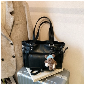 Macro detail of black leather tote bag with vintage metal buckle and cute bear charm