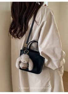 Minimalist black leather crossbody bag featuring a plush rabbit charm and gold accents