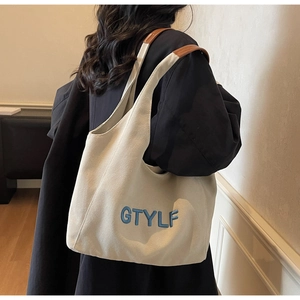 Detail of canvas tote bag with GTYLF embroidery and brown leather handles on shoulder