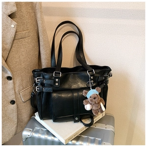 Detail of black leather tote bag with silver buckles and cute plush bear charm
