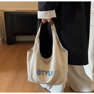 Detail of off-white canvas tote with blue GTYLF embroidery and brown leather handle accents