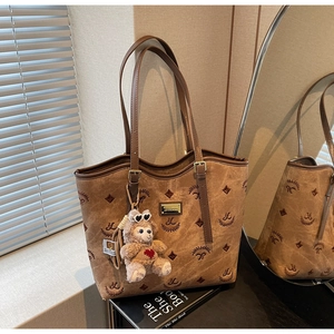 Detail of suede tote bag with brown embroidery, metal buckle, and plush charm