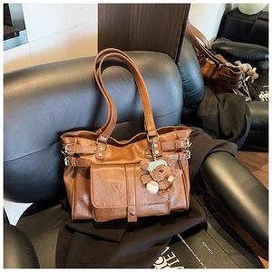 Detailed view of a brown vintage leather tote with a large front pocket and bear charm