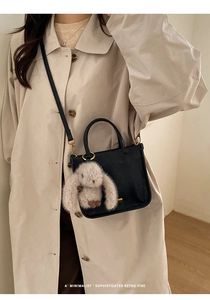 Detail of black pebbled leather mini handbag with a plush rabbit charm and gold hardware