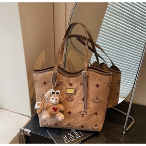 Detail of vintage brown monogram tote bag with a cute teddy bear charm on a wood table