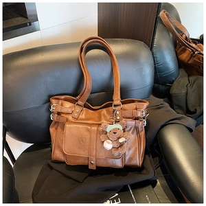 Detail of vintage brown tote bag with metal buckles and plush bear charm on black sofa