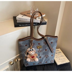Detail of vintage denim tote bag with leather trim and plush bear charm on a chair