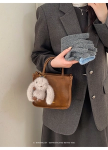 Détail du sac seau rétro en cuir marron avec charm lapin en peluche et écharpe en maille