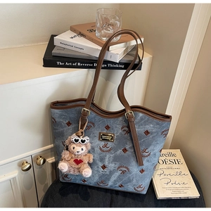 Close-up of blue denim tote bag with brown embroidery and cute plush bear charm accessory