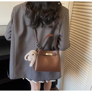 Detail of brown litchi grain leather bucket bag with gold clasp and plush bunny charm