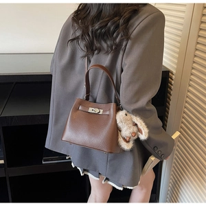 Brown lychee leather bucket bag with silver clasp and plush bunny charm on a grey suit
