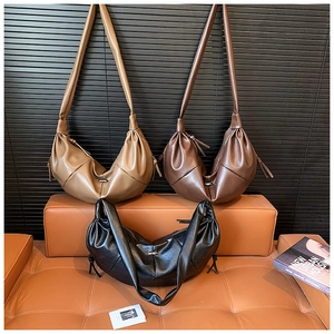 Three pleated crescent shoulder bags in khaki, brown and black on a leather sofa