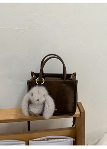 Close-up of deep brown bucket bag texture with a cute grey plush rabbit pendant accessory