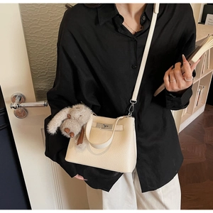 Detail of cream white pebbled leather bucket bag with metal turn-lock and rabbit plush charm