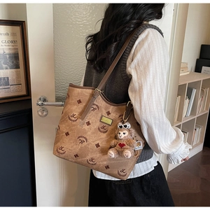 Detailed side view of vintage brown monogram tote bag with cute plush bear charm