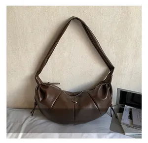 Detail view of the pleat design and silver metal piece on a dark brown hobo bag