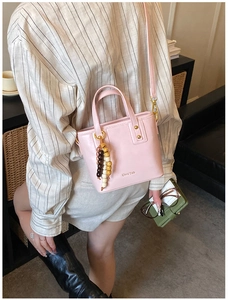 Detail of a pink bucket bag with a wooden bead tassel worn crossbody on a striped shirt