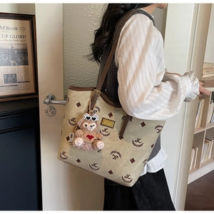 Detail of a large khaki tote bag with monogram patterns and a brown bear plush charm